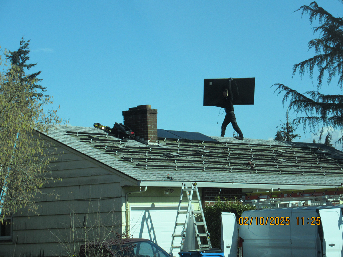 A worker carrying a solar panel on a roof without fall protection.